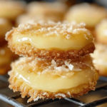 A plate of heavenly coconut lemon curd cookies, featuring a soft, golden coconut cookie with a bright yellow lemon curd center and a dusting of powdered sugar.