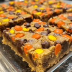 A batch of Reese’s Pieces chocolate chip cookie bars, featuring golden, gooey cookies studded with colorful Reese’s Pieces, served on a rustic plate.