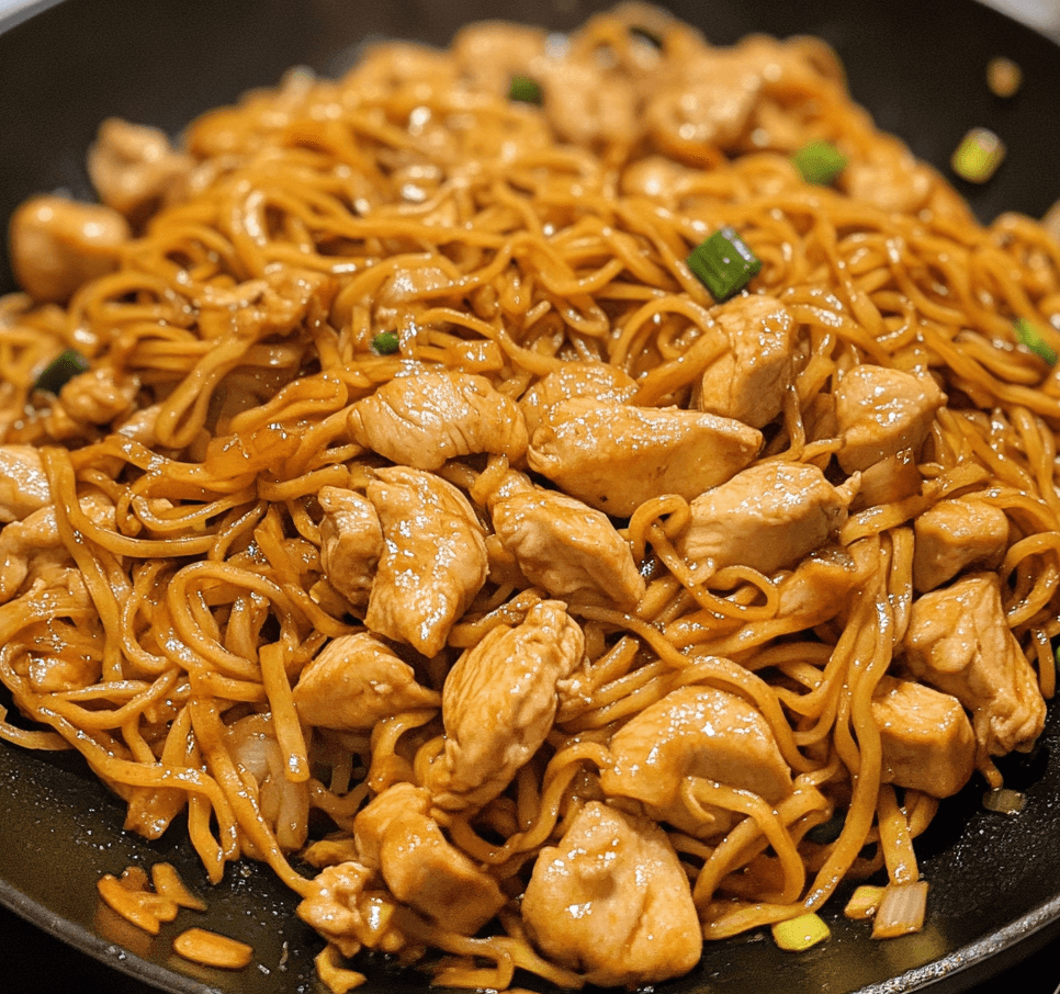 A plate of chicken chow mein stir-fried with vegetables and noodles, garnished with green onions and sesame seeds.