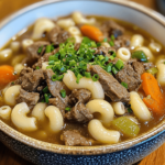 A steaming bowl of beef and macaroni soup, featuring tender ground beef, macaroni pasta, diced tomatoes, and fresh herbs in a savory broth.