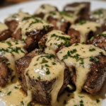 A plate of garlic butter steak bites, golden and crispy on the outside, drenched in a creamy parmesan sauce, garnished with fresh herbs.