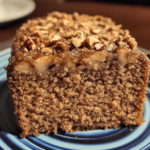 A slice of apple walnut spice cake with visible apple chunks and walnuts, topped with a dusting of powdered sugar and surrounded by autumn-themed decorations.