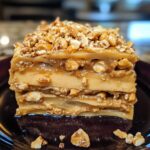 A slice of peanut butter crunch lasagna, with layers of creamy peanut butter filling, a chocolate topping, and crunchy layers, served on a dessert plate.