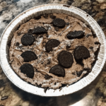 Oreo Mud Pie with a chocolate cookie crust, layers of chocolate pudding, whipped cream, and crushed Oreos, garnished with a whole Oreo on top.