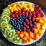 Rainbow Fruit Platter featuring a colorful arrangement of fresh fruits, including strawberries, oranges, pineapple, kiwi, blueberries, and grapes, displayed on a large white platter.