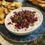 Holiday Cranberry Jalapeño Cream Cheese Dip in a festive bowl, topped with cranberry sauce and jalapeño slices, served with crackers and fresh herbs for garnish.