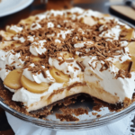 Banoffee Pie with a golden biscuit crust, layers of caramel, fresh banana slices, and whipped cream, topped with chocolate shavings for a decadent finish.