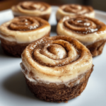 Cinnamon Roll Mini Cheesecakes with a cinnamon-spiced crust, creamy filling, and a swirl of cinnamon sugar, topped with a drizzle of icing on a rustic tray.